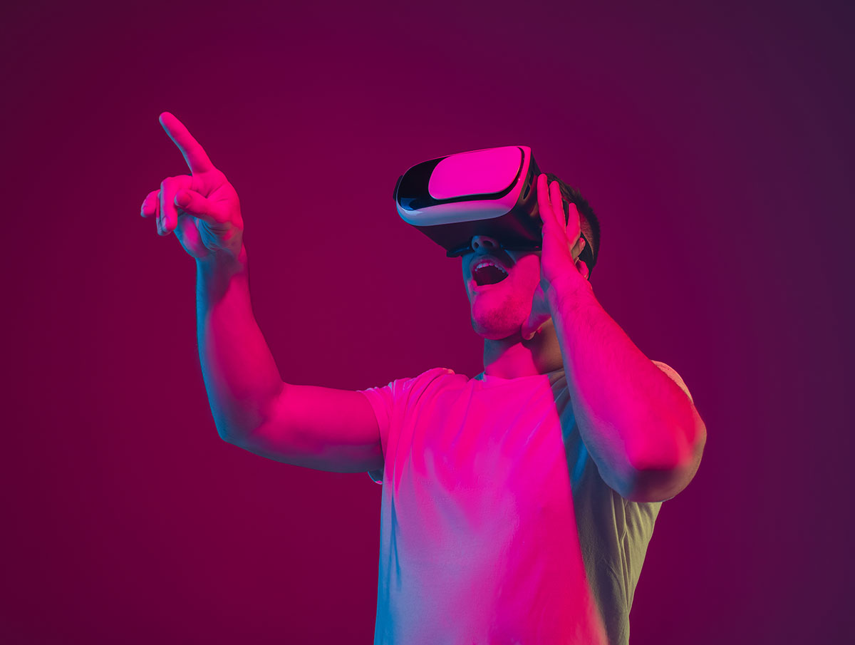 Caucasian man’s portrait isolated on pink-purple studio background in neon light, playing with VR-headset